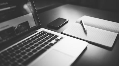 Apple MacBook on a desk with an iPhone and notepad