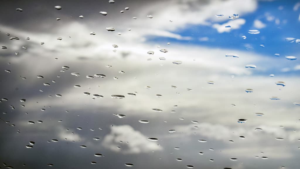 Rain on a window looking up at the sky with clouds.